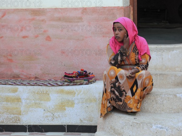 In a Nubian village, young girl with headscarf sitting on the ground, Egypt, Africa