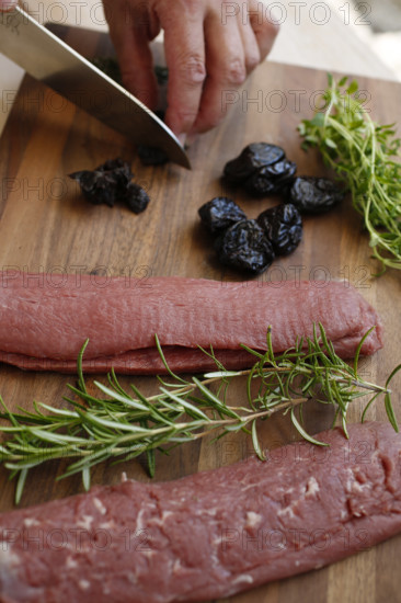 Swabian cuisine, preparation of lamb with prunes, raw lamb, rosemary, herbs, sliced garlic, lemon zest, fillets on wooden board, cutting prunes, kitchen knife, grandmother's kitchen, regional, home cooking, typical Swabian, traditional cuisine reinterpreted, food photography, man's hand, studio, Germany, Europe