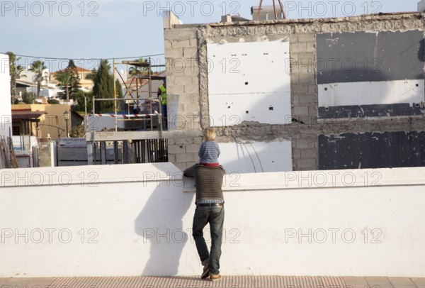 Child sitting on father's shoulders watching building site work, Fuerteventura, Canary Islands, Spain, Europe