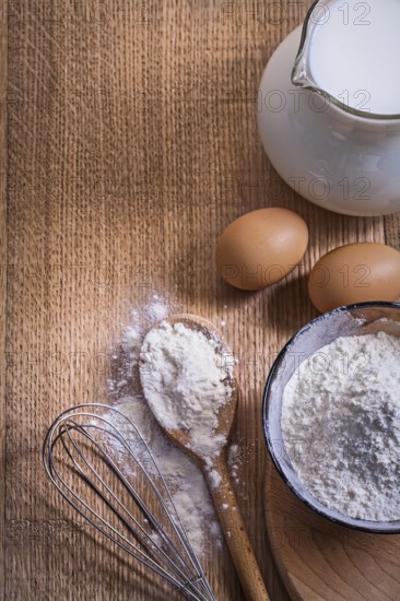 Aerial view copyspace composition pitcher with milk flour in bowl and spoon eggs corolla on wooden board food and drink concept