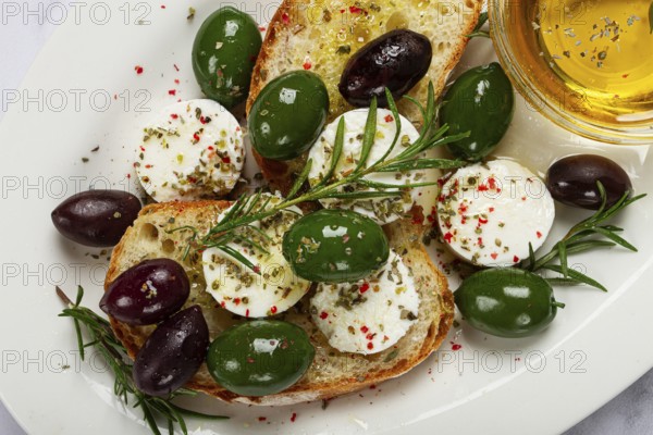 A plate with a snack, ciabatta bread with cheese and olives, olive oil, spices and herbs, top view, no people