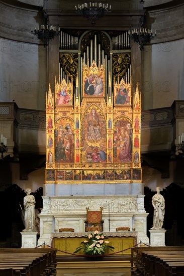 Montepulciano, Duomo (Cathedral of S. Maria Assunta), the interior, the main altar: the monumental "Triptych of the Assumption", painted by Taddeo di Bartolo in 1401. The central panel of the triptych shows the monumental figure of the Madonna Assunta surrounded by Angels, while below are visible the twelve apostles crowding around the empty tomb of the Madonna. Above the Assumption we see the Coronation of the Virgin. The three scenes must be read as a time sequence from bottom to top with the Death of the Virgin, her Assumption and her Coronation. The two side panels depict various Saints in the attitude of adoring the central figure of the Madonna, while on the four pillars that delimit the various panels we see twelve small figures of Doctors of the Church (three per pillar). Above the two side panels are the Announcing Angel (on the left) and the Madonna Annunziata (on the right). The predella at the bottom depicts Nine scenes from the life of Jesus Christ while above the predella...