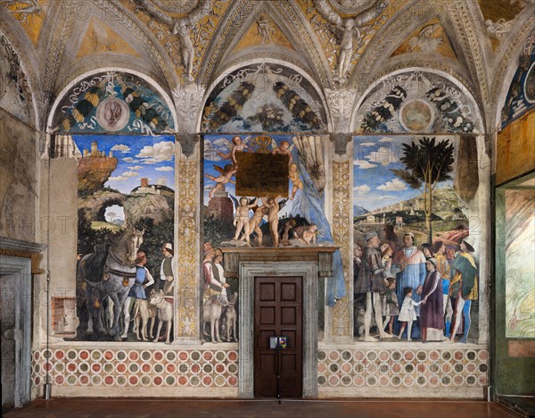 Ducal Palace: south-west wall of the “Bridal Chamber or Camera Picta", which is a room located in the north-east tower of the Castle of San Giorgio in Mantua. It is famous for the cycle of frescoes that covers its walls, a masterpiece by Andrea Mantegna, created between 1465 and 1474.
The wall, on the theme of “The Meeting” is divided into three sectors. In the one on the left the actual meeting takes place, in the central one some cherubs hold a dedicatory plaque and in the one on the right the marquis's court parades.
The Marquis Ludovico is represented in the Meeting, this time in official guise, perhaps flanked by Ugolotto Gonzaga, son of his deceased brother Carlo. His son Francesco who is a Cardinal is in front of him. Below them are the sons of Federico I Gonzaga, Francesco and Sigismondo, while their father Federico is on the far right: the generous folds of his dress are a ploy to hide his kyphosis. Federico is in conversation with two characters, one in front and the other ...