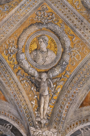 Ducal Palace: vault of the “Bridal Chamber or Camera Picta", which is a room located in the north-east tower of the Castle of San Giorgio in Mantua. It is famous for the cycle of frescoes that covers its walls, a masterpiece by Andrea Mantegna, created between 1465 and 1474.
Detail of the vault: lozenge with a golden background that encloses a circular garland which in turn encloses the portrait of the Roman emperor "Otho". The garland is supported by a putto.
Palazzo Ducale, Mantova (MN) - Mantua, Lombardia - Lombardy, Italia - Italy