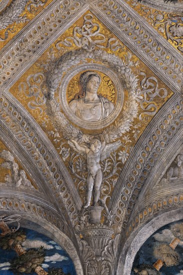 Ducal Palace: vault of the “Bridal Chamber or Camera Picta", which is a room located in the north-east tower of the Castle of San Giorgio in Mantua. It is famous for the cycle of frescoes that covers its walls, a masterpiece by Andrea Mantegna, created between 1465 and 1474.
Detail of the vault: lozenge with a golden background that encloses a circular garland which in turn encloses the portrait of the Roman emperor “Julius Caesar”. The garland is supported by a putto.
Palazzo Ducale, Mantova (MN) - Mantua, Lombardia - Lombardy, Italia - Italy