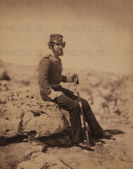 British Lieutenant John Sherwood Gaynor, 47th (Lancashire) Regiment of Foot, Full-Length Portrait Wearing Uniform, Holding Sword, Sitting on Rock, Crimean War, Crimea, Ukraine, by Roger Fenton, 1855