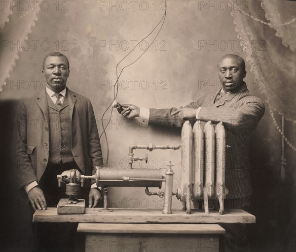 American inventor Charles S.L. Baker (right), standing behind heating radiator, system, Martin W. Bode, 1906