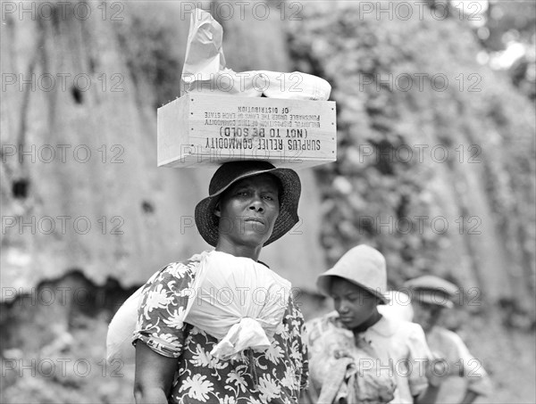 Woman transporting packages  of surplus  relief commodities, a New Deal government program, on her head and over shoulder,  Natchez, Mississippi, USA, Marion Post Wolcott, U.S. Farm Security Administration, August 1940