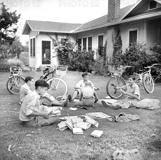 Group of boys folding newspapers on front yard lawn before delivering them in the afternoon, Natchitoches, Louisiana, USA, Marion Post Wolcott, U.S. Farm Security Administration, June 1940