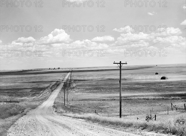 Dirt road through rural landscape with grain elevators in background, Homestead, Montana, USA, Marion Post Wolcott, U.S. Farm Security Administration, August 1941