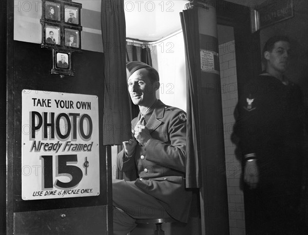 Man in military uniform sitting in  picture-taking machine in lobby at United Nations service center, Washington, D.C., USA, Esther Bubley, U.S. Office of War Information, December 1943