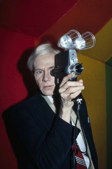 American pop artist Andy Warhol, half-length portrait looking through lens of Polaroid Polavision camera, Bernard Gotfryd, 1977