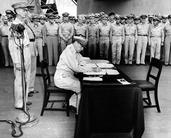 U.S. General Douglas MacArthur seated at desk during formal surrender ceremonies aboard USS Missouri as soldiers look on, Tokyo Bay, Japan, U.S. Army Signal Corps, September 2, 1945