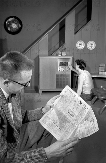 Man reading newspaper while woman is turning radio dial in living room, Warren K. Leffler, U.S. News & World Report Magazine Photograph Collection, 1957