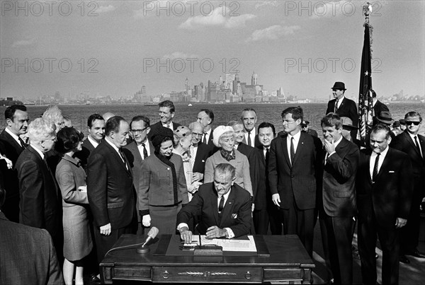 U.S. President Lyndon B. Johnson signing the Immigration and Nationality Act of 1965 as U.S. Vice President Hubert Humphrey, Lady Bird Johnson, Muriel Humphrey, Senator Edward Kennedy Senator Robert Kennedy, and others look on, Liberty Island, New York City, New York, USA, Yoichi Okamoto, October 3, 1965