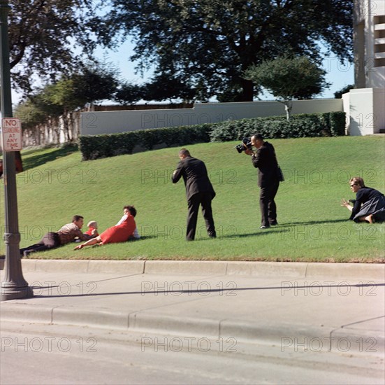 Witnesses laying down in grass immediately following assassination of U.S. President John Kennedy. Bill and Gayle Newman cover their children, Clayton and Billy (hidden) at left, photographers, including White House Motion Picture Photographer, Lieutenant Thomas M. Atkins (right), film in center, Dealey Plaza, Dallas, Texas, USA, Cecil Stoughton, White House Photographs, November 22, 1963