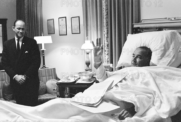 Paul Glynn looking on as U.S. President Lyndon Johnson giving OK sign from his hospital bed following throat polyp removal surgery, National Naval Medical Center, Bethesda, Maryland, USA, Robert Knudsen, November 16, 1966