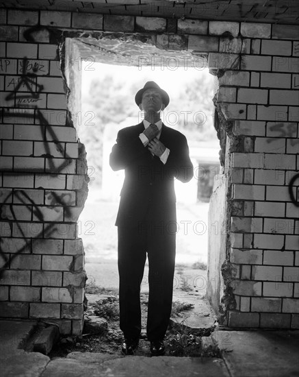 Mid-adult man in suit and hat adjusting tie while standing in open doorway