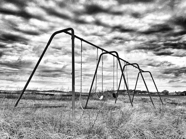 Swing set in field with long grass and dramatic sky