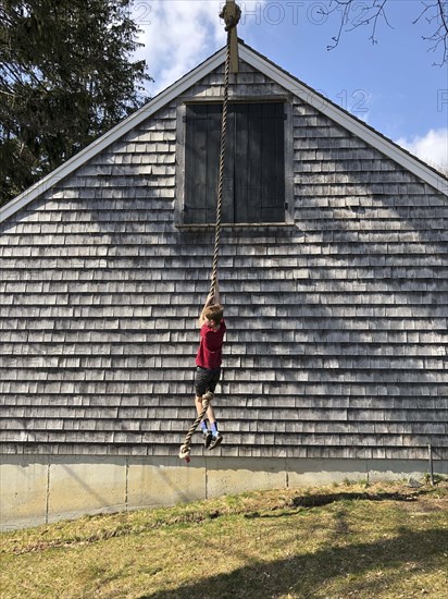 Young boy climbing on rope hanging from barn