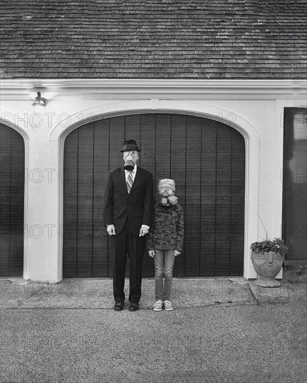 Full-length portrait of mid-adult businessman and teen boy wearing gas masks in front of garage door