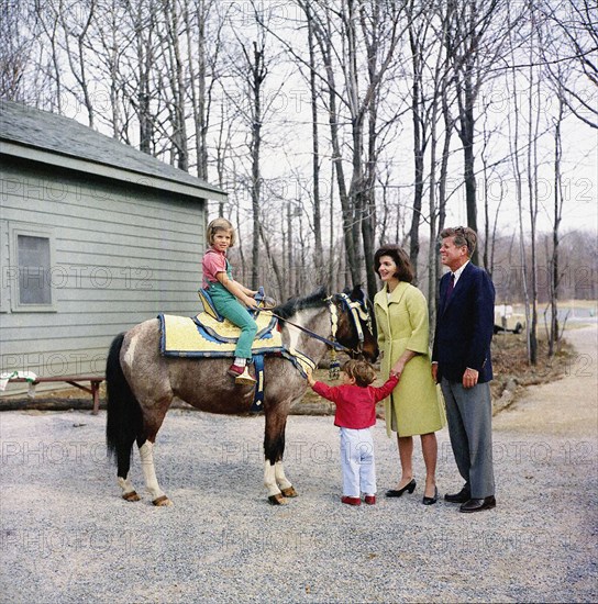 U.S. President John F. Kennedy and U.S. First Lady Jacqueline Kennedy stand with their children, Caroline Kennedy, sitting on her pony, "Macaroni", and John F. Kennedy, Jr., Camp David, Frederick County, Maryland, USA, Robert Knudsen, White House Photographs, March 31, 1963