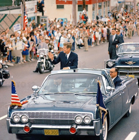 U.S. President John F. Kennedy (standing in first car) with Governor of California, Edmund G. "Pat" Brown (seated in back seat), waving from open convertible, Governor of California, Edmund G. "Pat" Brown (seated in back seat  as his motorcade traveled through San Diego, California, USA, Cecil Stoughton, White House Photographs, June 6, 1963