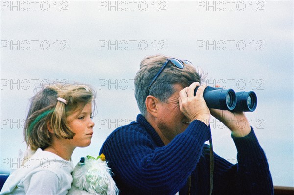 U.S. President John F. Kennedy looking through binoculars while sitting next to his daughter, Caroline Kennedy, aboard the Presidential yacht, “Honey Fitz,” off the coast of Hyannis Port, Massachusetts, USA, Cecil Stoughton, White House Photographs, August 25, 1963