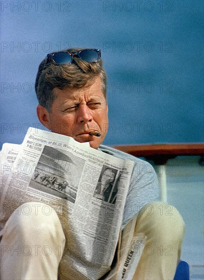 U.S. President John F. Kennedy smoking cigar and reading newspaper while sitting aboard Presidential yacht, “Honey Fitz,” during Labor Day weekend, Hyannis Port, Massachusetts, USA, Cecil Stoughton, White House Photographs, August 31, 1963