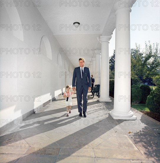 U.S. President John F. Kennedy walking with his son, John F. Kennedy, Jr. (carrying a soda bottle), along West Wing Colonnade of White House, Washington, D.C., USA, Robert Knudsen, White House Photographs, October 7, 1963