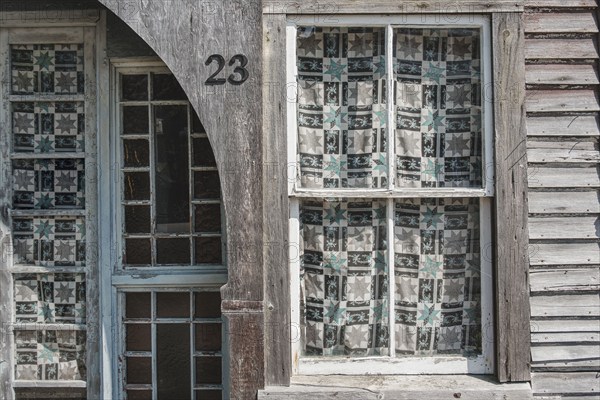 Weathered building exterior with pane windows covered in patterned curtains