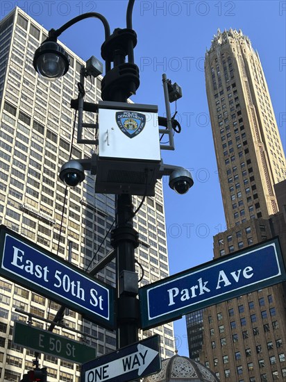 Low angle view of two office buildings with police security cameras attached to lamppost with street signs at East 50th Street and Park Avenue, New York City, New York, USA