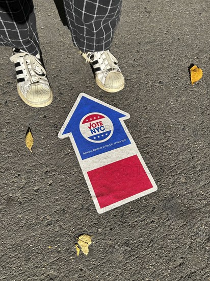 High angle view of person standing near NYC board of elections early voting arrow sign adhered to pavement, New York City, New York, USA