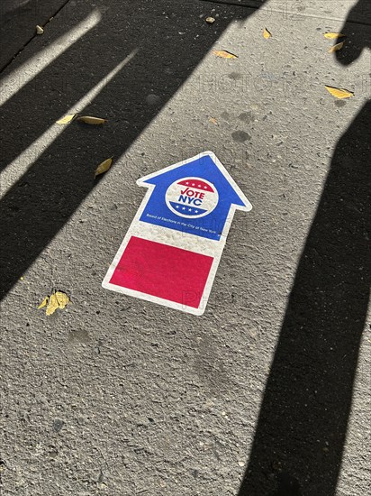 High angle view of human shadows near NYC board of elections early voting arrow sign adhered to pavement, New York City, New York, USA