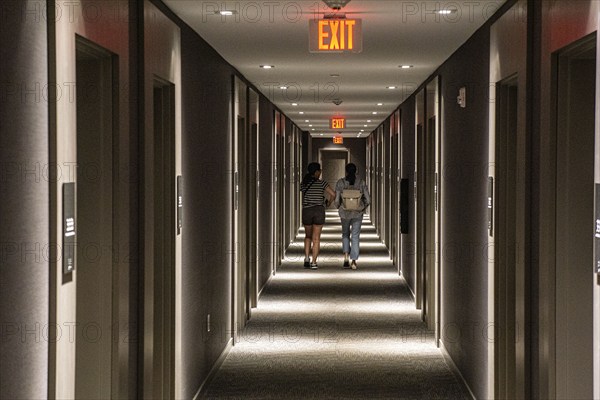 Rear view of two people walking down hotel hallway, diminishing perspective