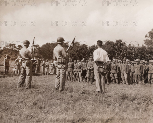 Japanese soldiers line up for formal surrender ceremonies as U.S. Marines with tommy guns and fixed bayonets stand guard, Motobu Peninsula, Okinawa, W. Huntington, U.S. Marine Corps, September 2, 1945