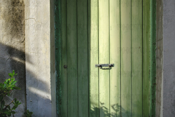 Old green wood door with center black metal handle in shadow