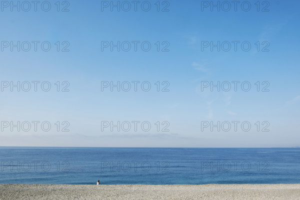 Rear view of solitary woman sitting on beach and looking out to sea