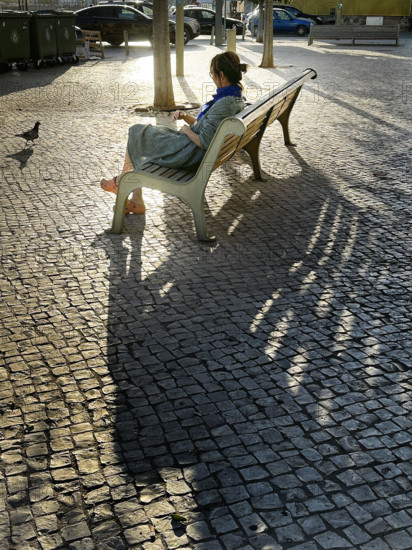 Woman sitting in shadows on park bench in urban landscape, Alcacer do Sal, Portugal