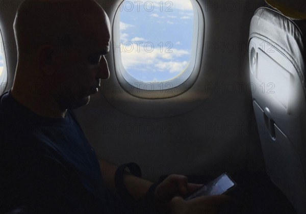 Silhouette of mid-adult man looking at his smartphone on airplane