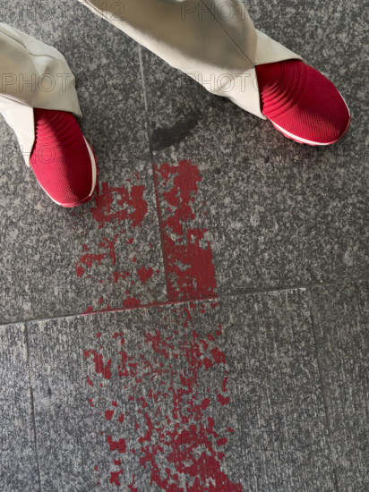 high angle view of red sneakers near a splatter of red paint on granite floor tiles