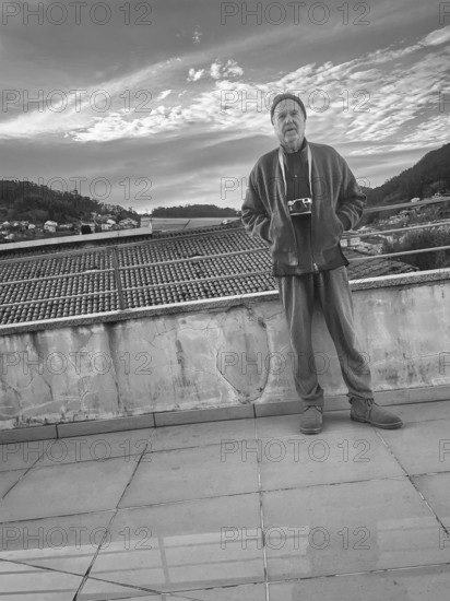 Full-length portrait of mature adult man standing on bridge overlooking rooftops, Bueu, Spain