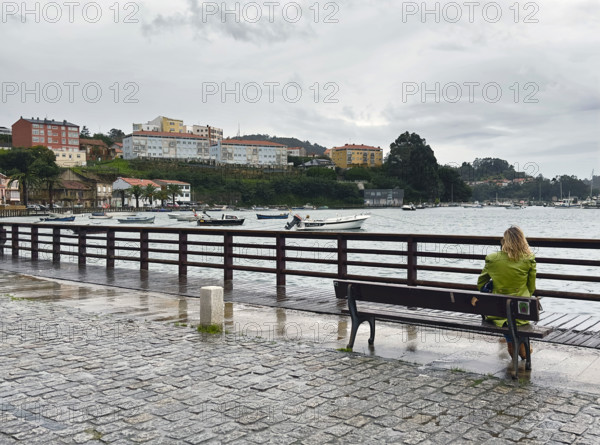 Rear view of woman sitting on bench looking at boats in harbor, Mugardos, Galicia, Spain