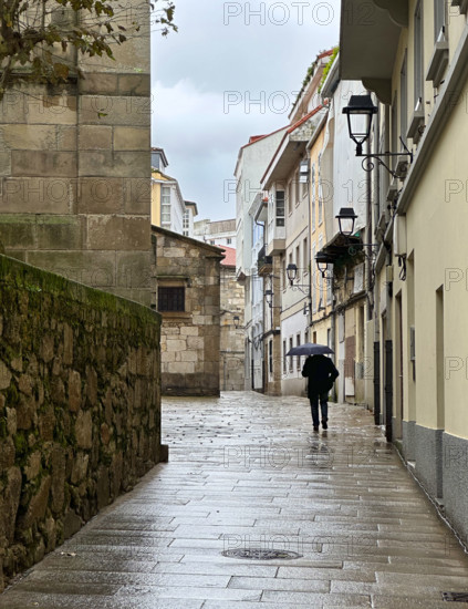 Man with umbrella walking through quaint town on rainy day, A Coruña, Galicia, Spain