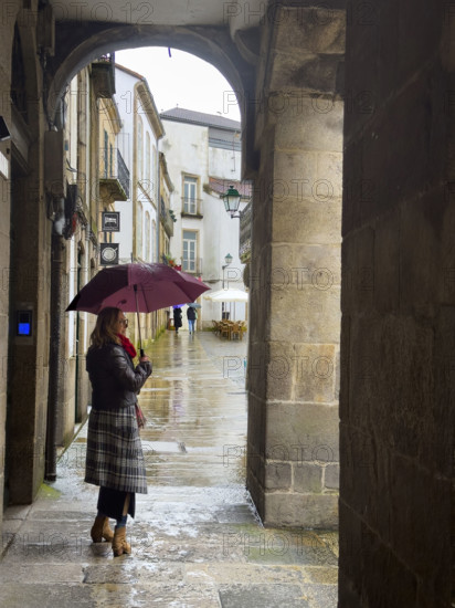 Woman with umbrella in village square on rainy day, Santiago de Compostela, Galicia, Spain