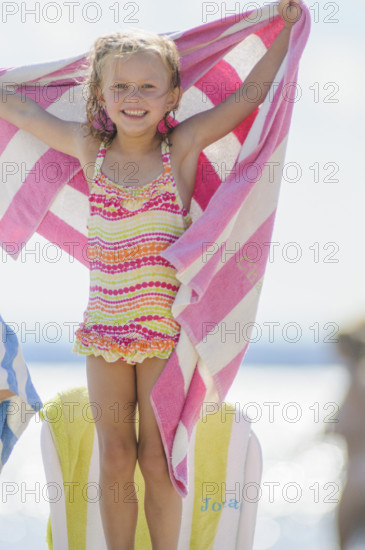 Smiling young girl holding up towel with pink stripes at beach