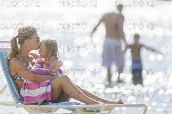 Mother kissing young daughter on forehead in foreground, father wading into water with son in background