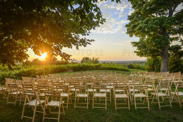 Rows of wood folding chairs set up for outdoor event at sunset