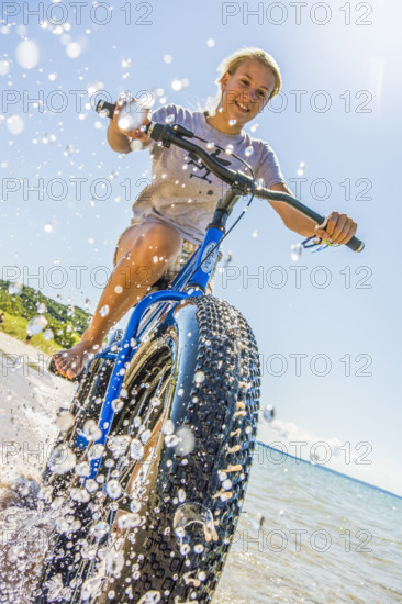 Young teen girl riding bicycle through water at beach