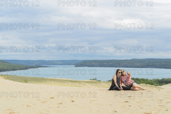 Mother and daughter taking a selfie atop sand dunes at beach